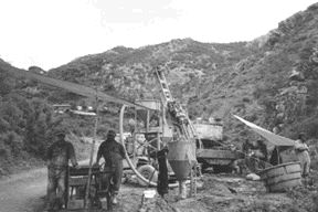 COLOUR PIC -- FPODrillers stand near a reverse-circulation drill on the Dolores Main zone. Another core rig turns on the ridge in the background. The property consists of nine concessions totalling 277 sq. km. Seven of the concessions comprise 19 sq. km covering the core of the Dolores district. Minefinders can purchase a 100% interest in these concessions by paying a total of US$1.5 million at the rate of US$25,000 each quarter. So far, the company has paid US$942,000.