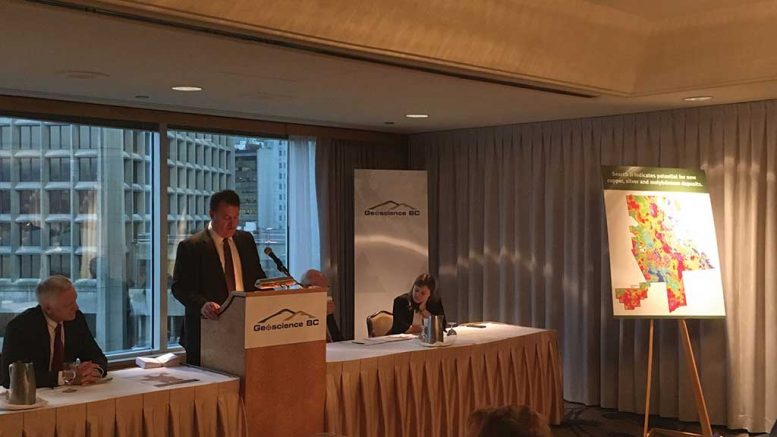 At the Geoscience BC presentation at the Association for Mineral Exploration’s Roundup convention in Vancouver, from left: Robin Archdekin, president and CEO of Geoscience BC; Bruce Madu, vice-president of minerals and mining at Geoscience BC; Bill Bennett, B.C.’s minister of energy and mines (behind podium); and Kendra Johnston, AME director. Photo by Lesley Stokes.