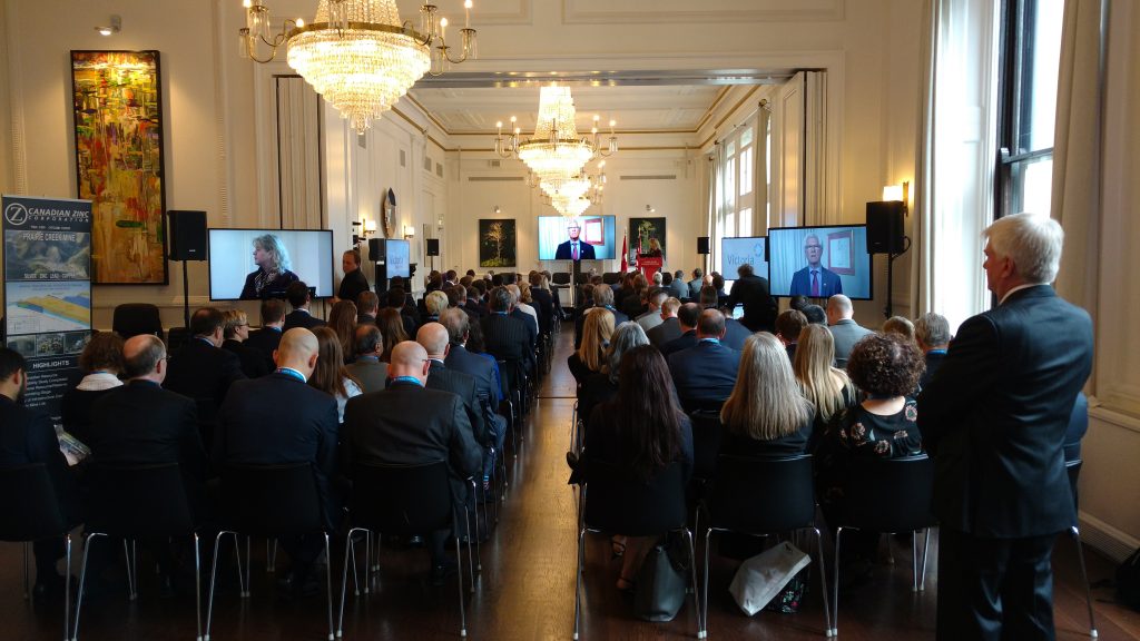 By video, Canada’s Minister of Natural Resources Jim Carr welcomes attendees of the Canadian Mining Symposium in Canada House in London, as Janice Charette, Canada’s High Commissioner to the U.K., stands at the podium. Photo by John Cumming.